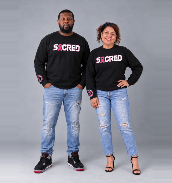 Twink and Anna wearing black Sacred Fight Cancer crewnecks with pink ribbon SACRED front designs and original sleeve logos
